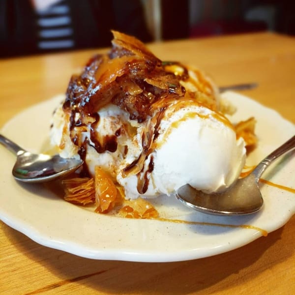 A dessert of vanilla ice cream topped with caramelized apples, chocolate, and caramel sauce.