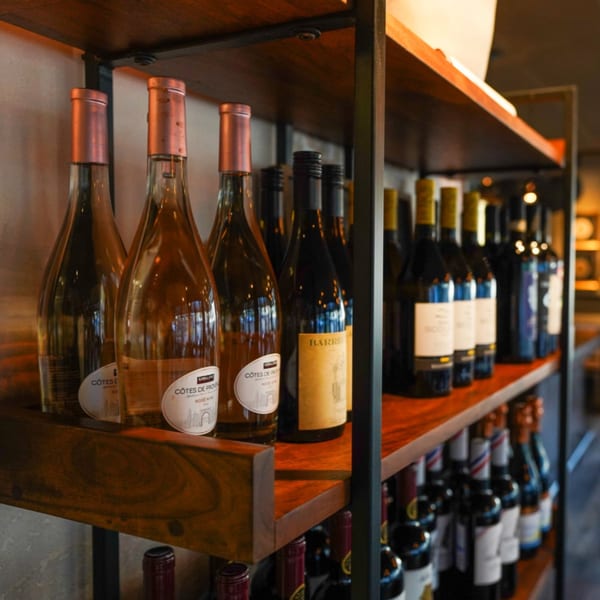 Wine bottles, including rosé and red, displayed on dark wooden shelves in a restaurant.