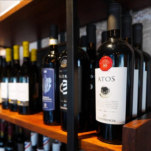 A close-up of various wine bottles, including an "ATOS" bottle with a red 99-point seal, on wooden shelves.