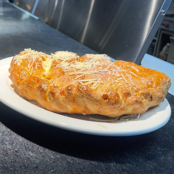 Golden-brown calzone topped with shredded cheese on a white plate, against a dark countertop.