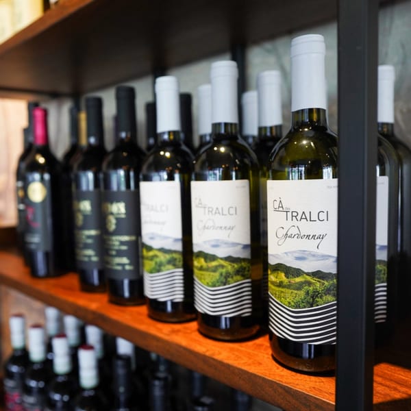 Wine bottles with white labels and green landscape designs displayed on wooden shelves.