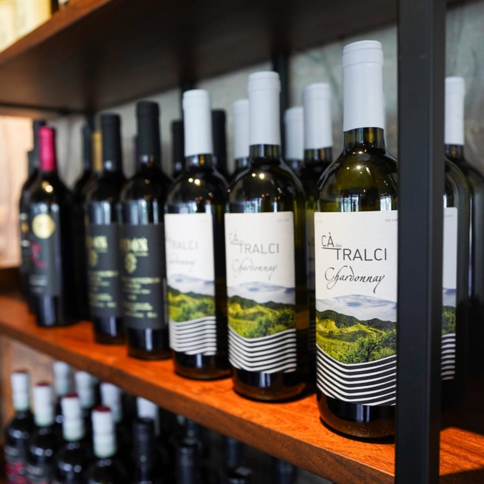 Wine bottles with white labels and green landscape designs displayed on wooden shelves.
