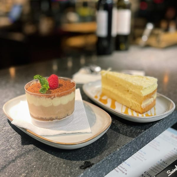 A tiramisu cup with raspberry and mint, and a slice of layered cake with syrup.