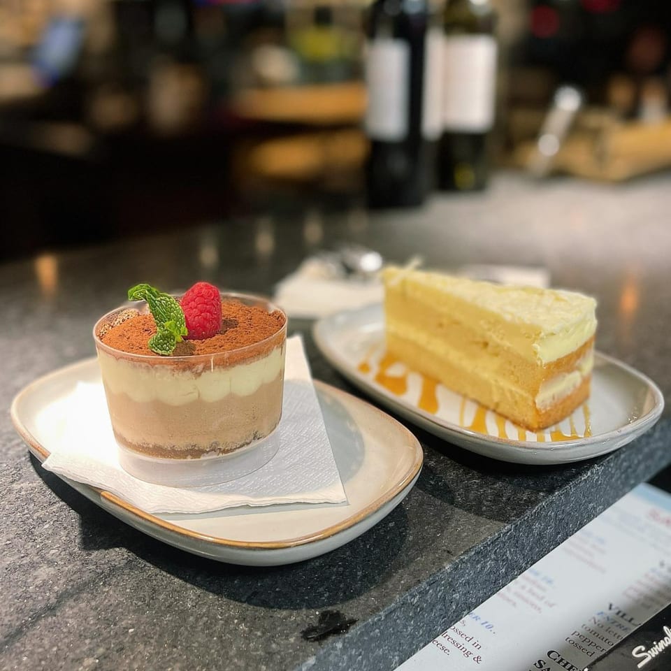 A tiramisu cup with raspberry and mint, and a slice of layered cake with syrup.