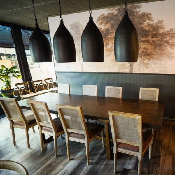 Long wooden dining table with chairs, dark pendant lights, and a tree mural in Olympia Pizza & Spaghetti House II.