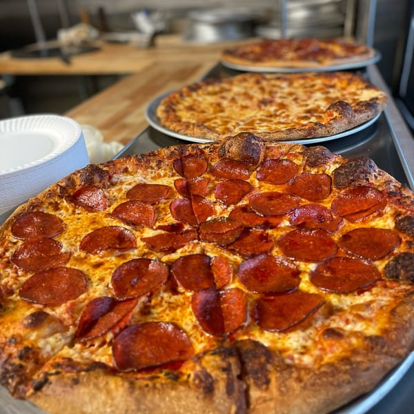 Three freshly baked Olympia Pizza & Spaghetti House II pizzas, with pepperoni in the foreground.