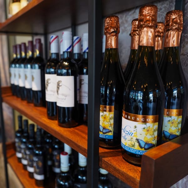 Wine bottles with decorative labels, including Lambrusco, displayed on wooden shelves at Olympia Pizza.