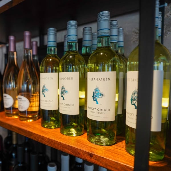 Bottles of Villa Loren Pinot Grigio and other wines displayed on a wooden shelf.